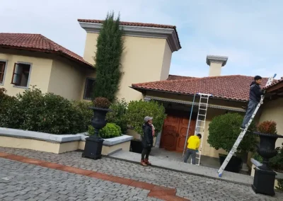 Reparación de techumbre en vivienda residencial con trabajadores realizando mantenimiento y ajuste de tejas en techo de casa en Santiago.